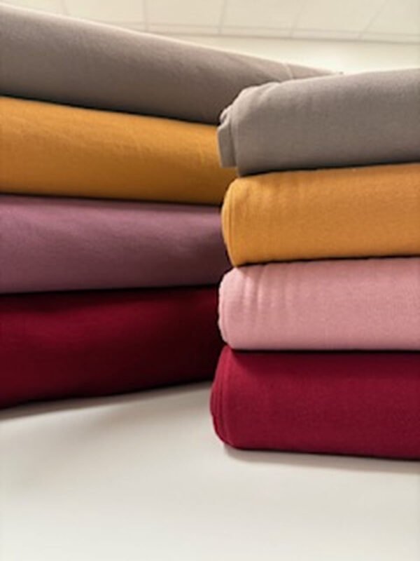 Barevné látky naskládané na stole, různé odstíny.