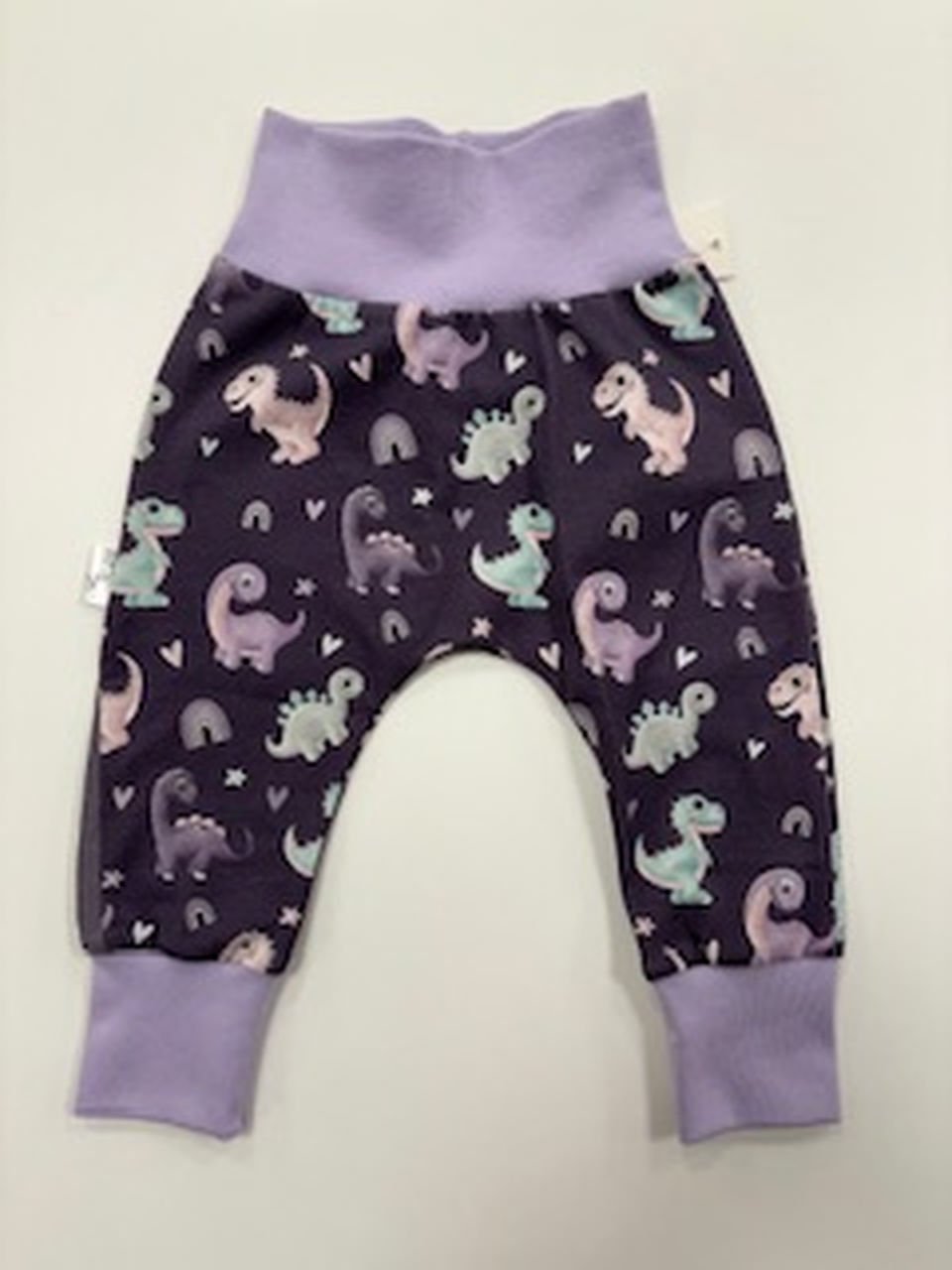 Dětské kalhoty s dinosaury na fialovém pozadí.
