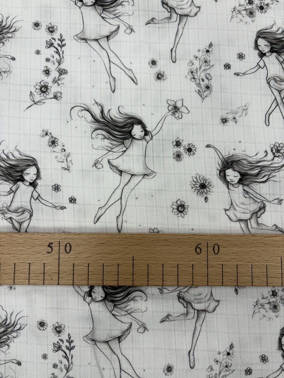Látka s vílami a květinami, dřevěné pravítko zobrazeno.
