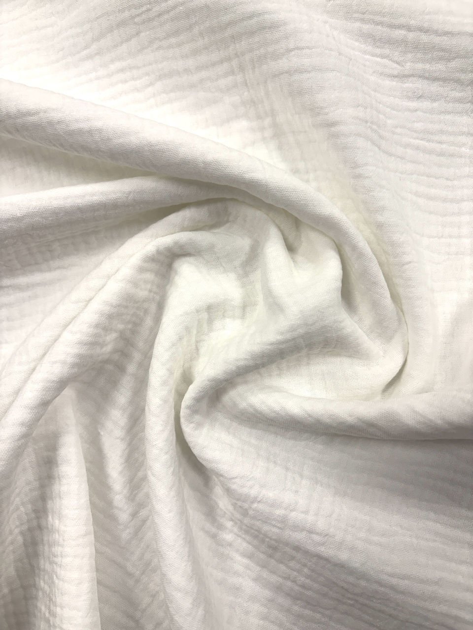 Bílá látka s jemnou texturou a záhyby.